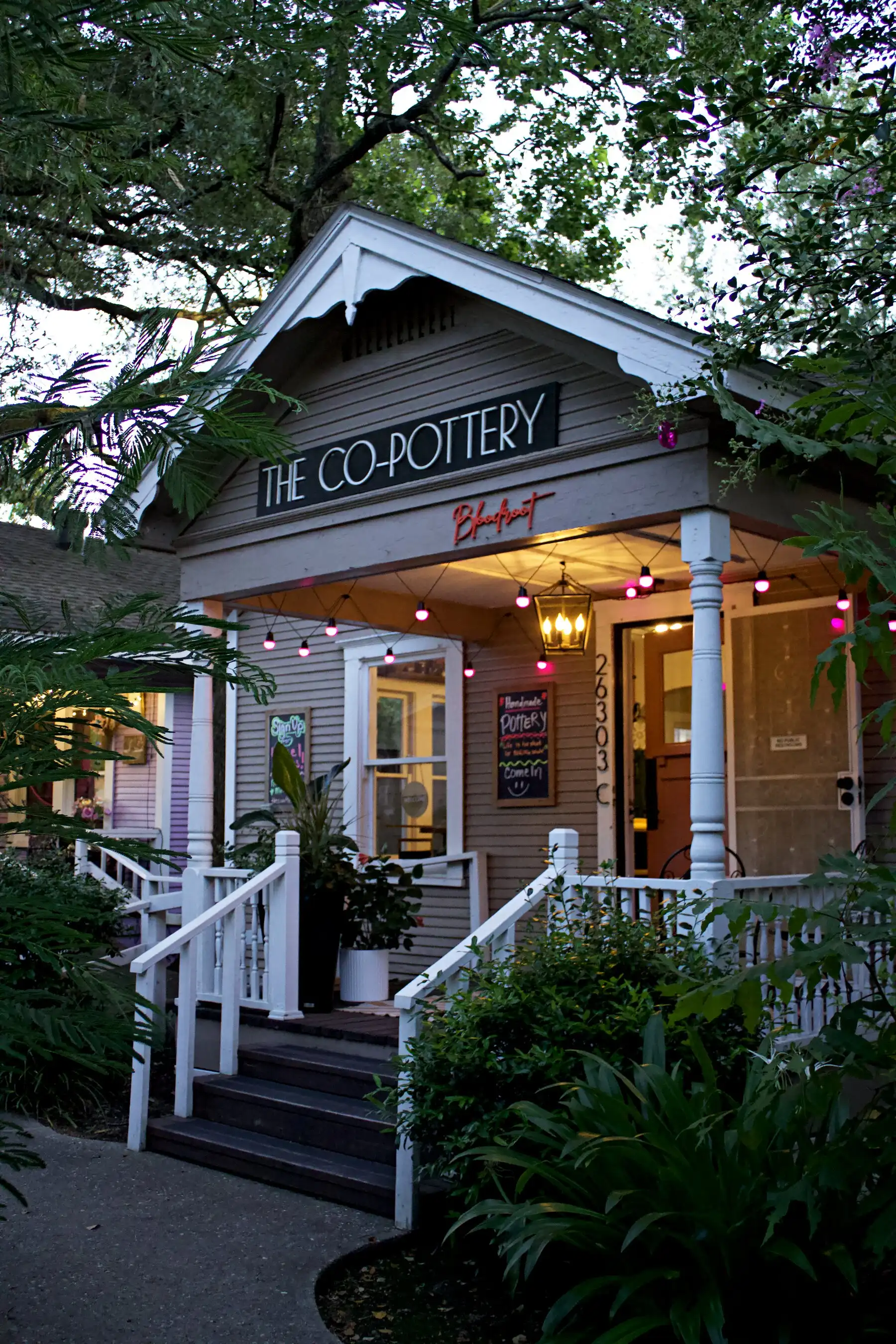 The Co-Pottery's cottage storefront at dusk, the porch glowing with string lights and a lantern